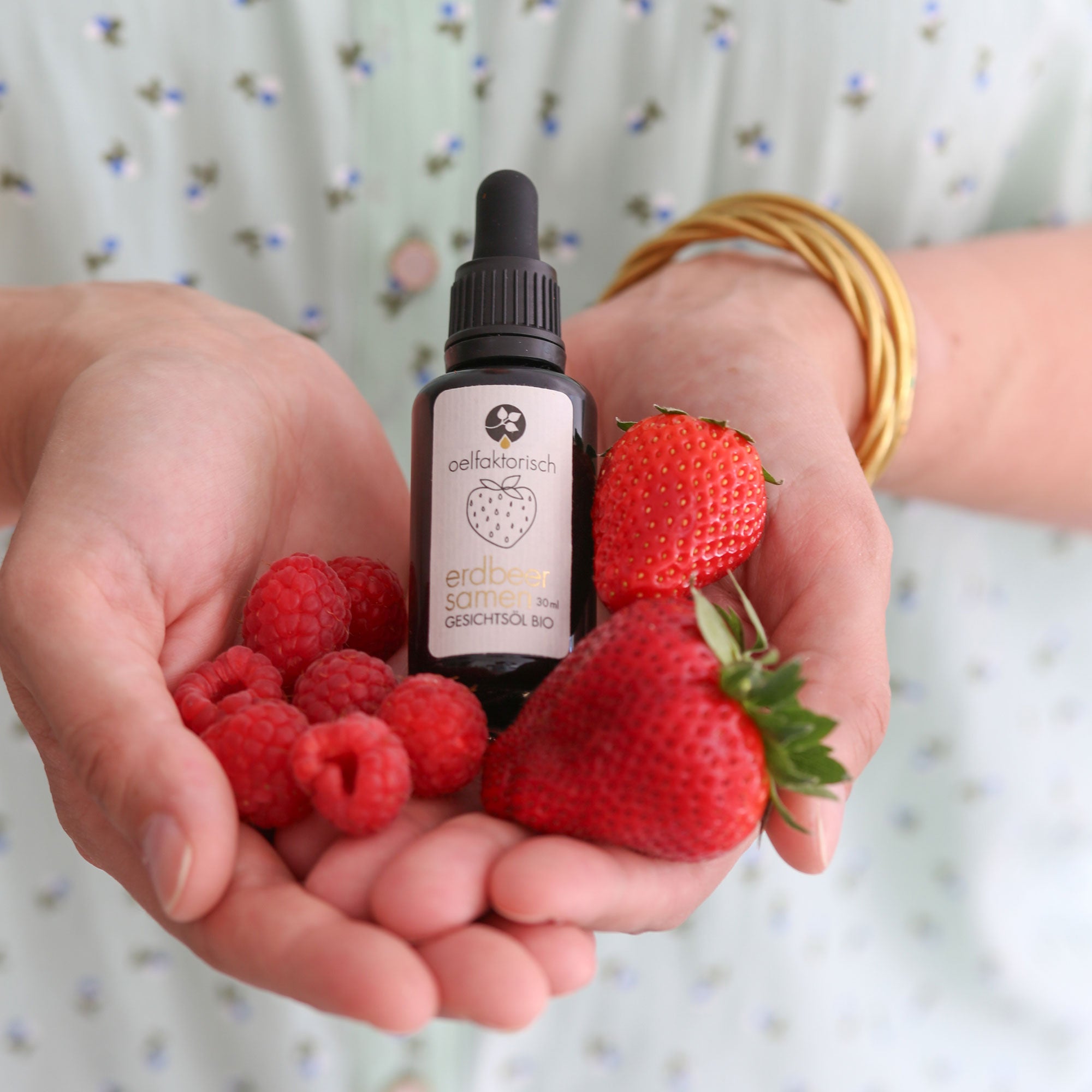 Hände mit erdbeersamen gesichtsöl und frischen Erdbeeren, pures Öl für das Gesicht mit Erdbeeren