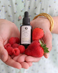 Hände mit erdbeersamen gesichtsöl und frischen Erdbeeren, pures Öl für das Gesicht mit Erdbeeren