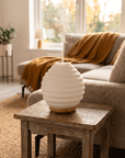 Weißer Diffuser Duftlampe Glas steht auf Beistelltisch neben Sofa elegant puristisch Raumbeduftung oelfaktorich körperöle